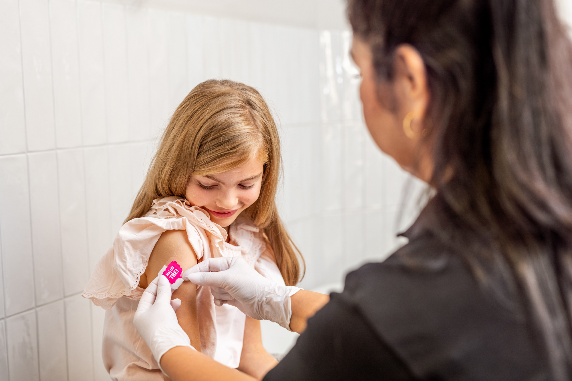Flicka får plåster på höger överarm från sjuksköterska efter vaccination