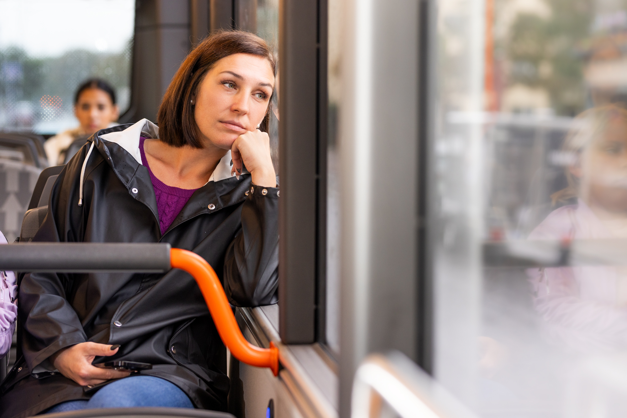 Ung kvinna åker buss – hon har en mobil i handen, men tittar ut genom fönstret