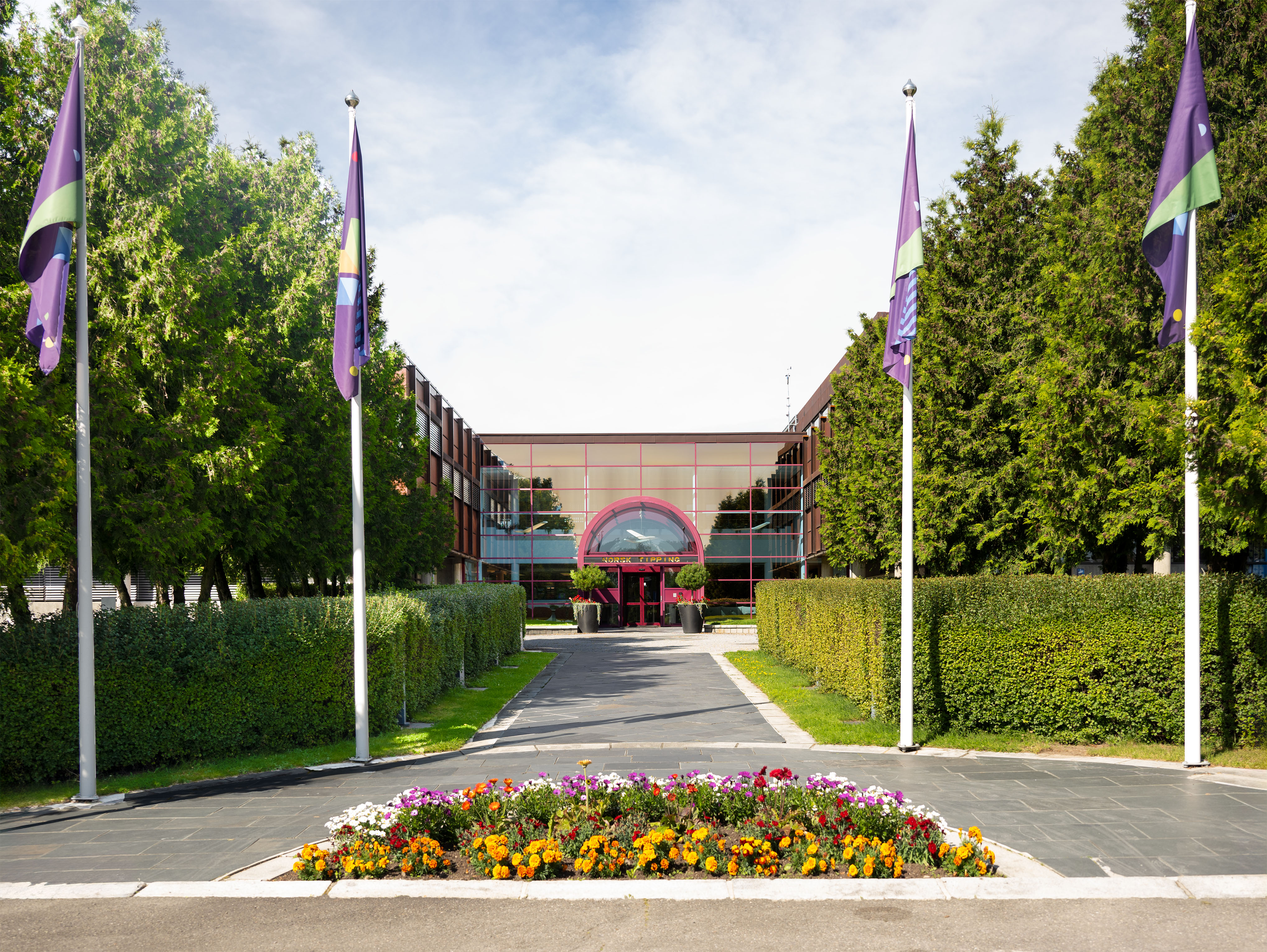 Hovedinngangen til Norsk Tipping med fargerike flagg og vakre blomster